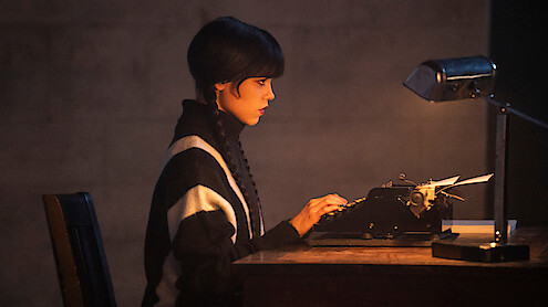 Jenna Ortega as Wednesday Addams sitting at a typewriter in the official Season 3 photograph